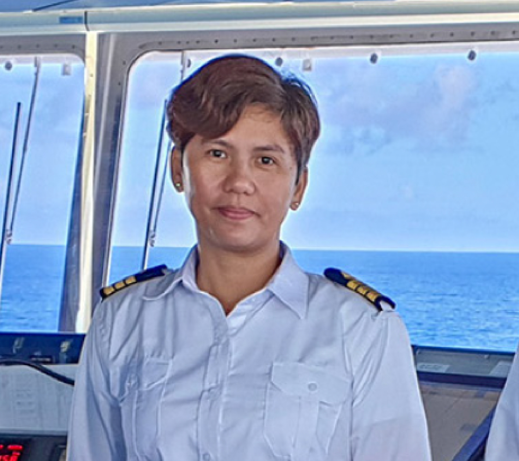 A female captain standing in the bridge of a vessel.