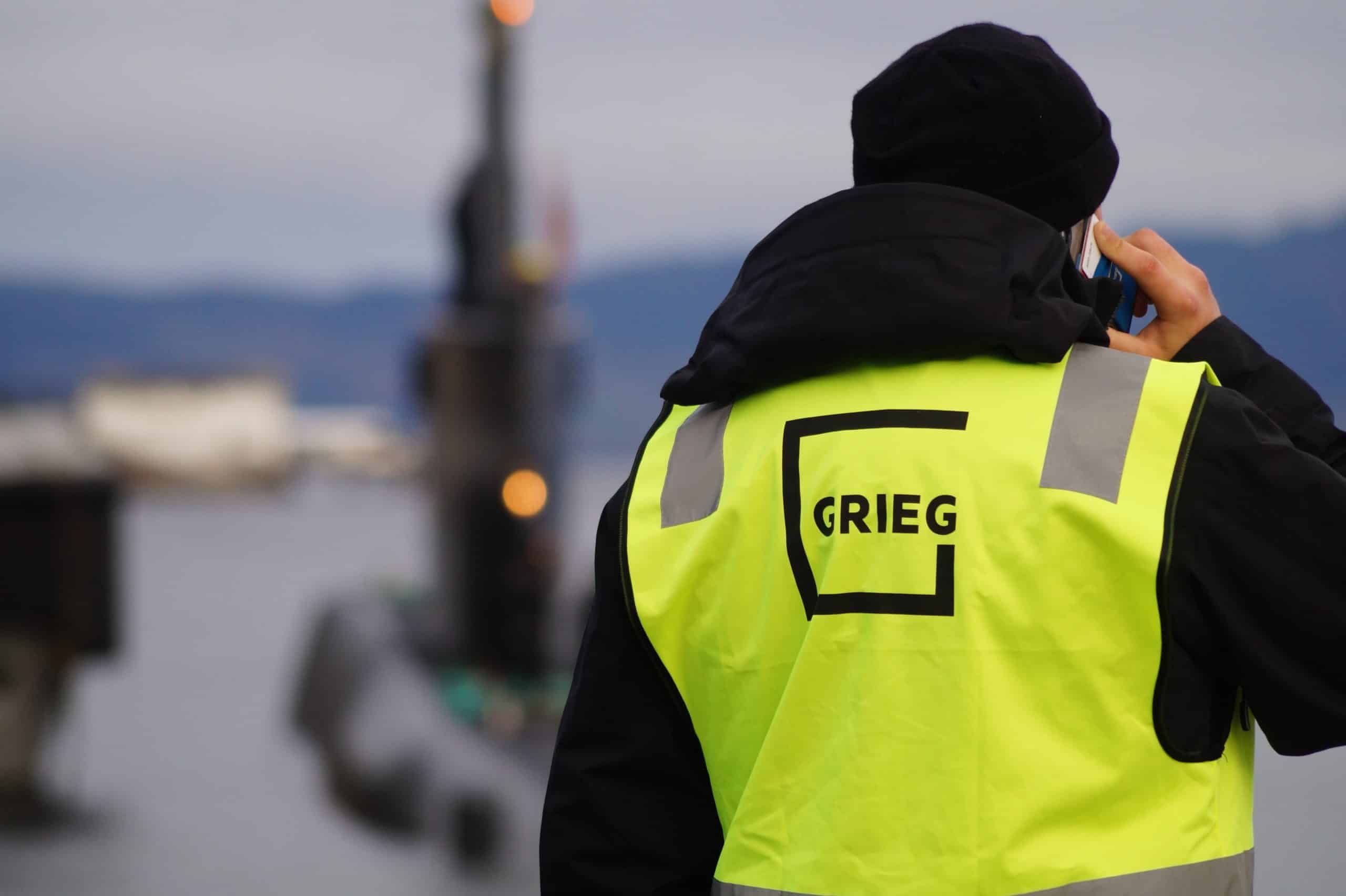 A man holding a phone, wearing a Grieg reflective vest.