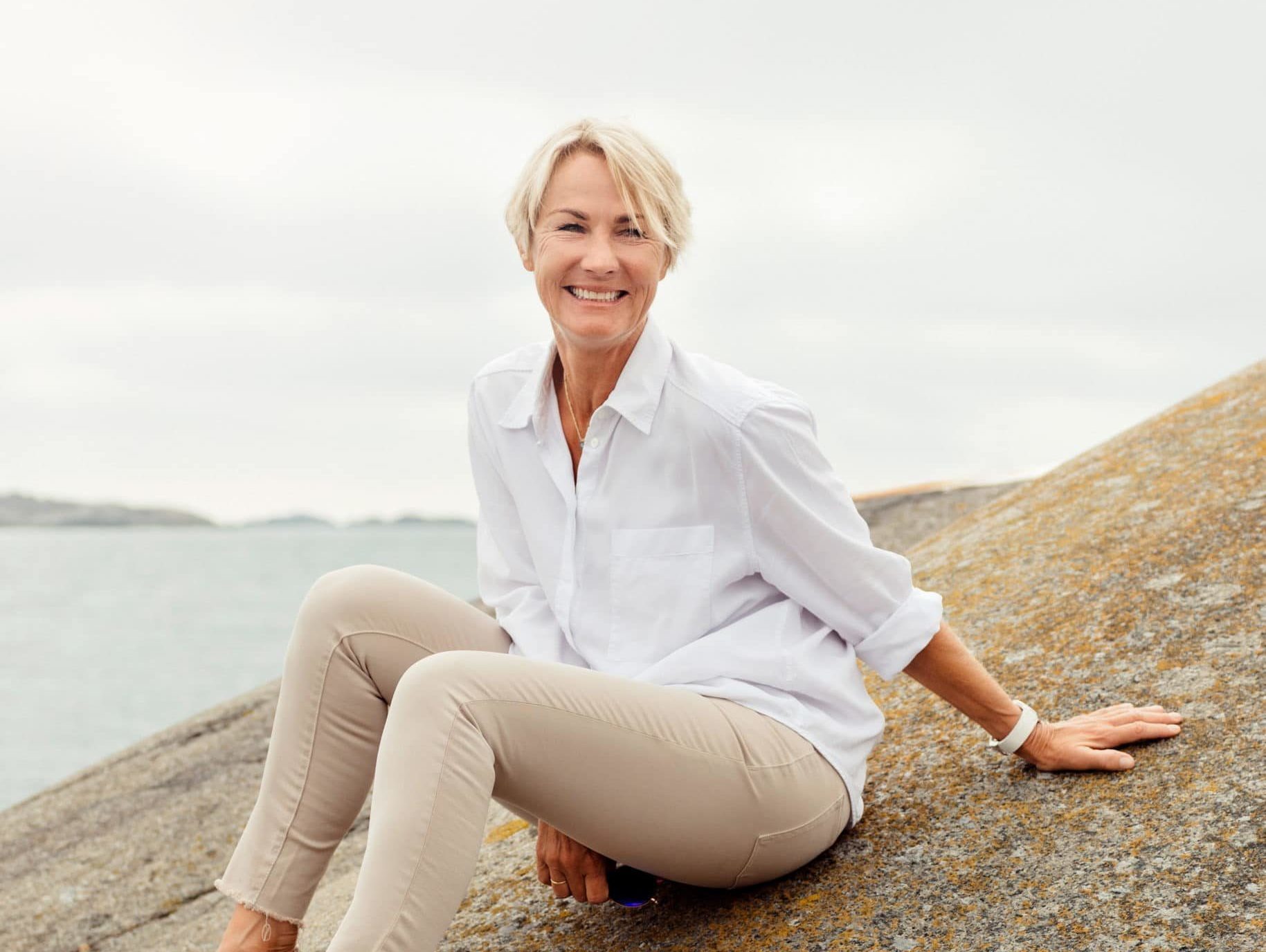 Elisabeth Grieg, the Chair of the board at Grieg, sitting on a rock by the ocean.